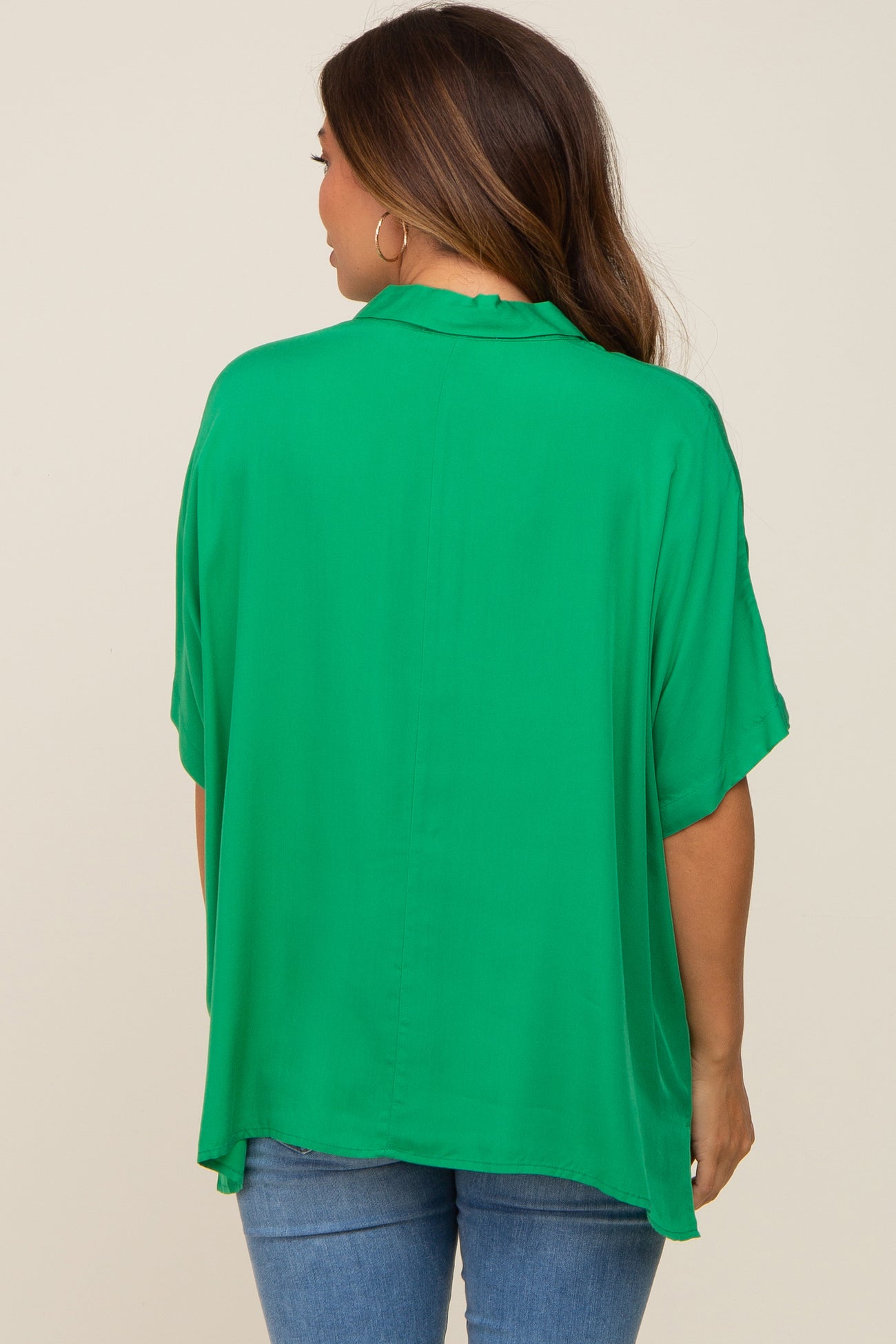 woman wearing a flowing green maternity top with a relaxed fit, seen from the back, paired with denim jeans