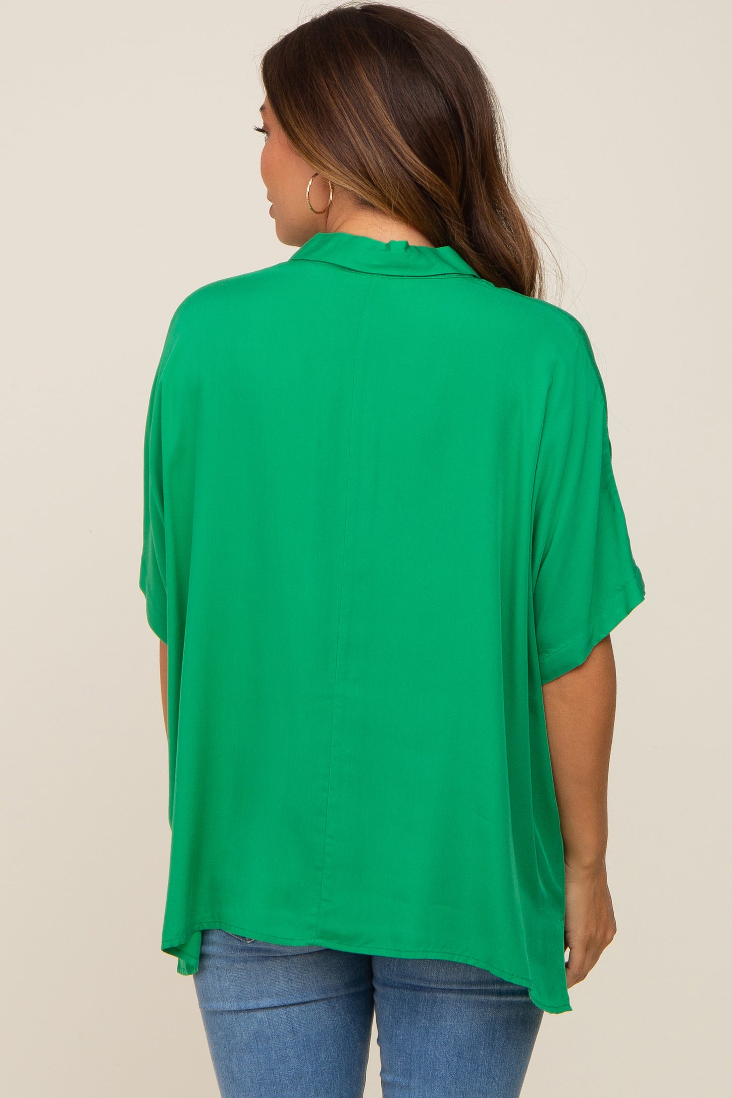 woman wearing a flowing green maternity top with a relaxed fit, seen from the back, paired with denim jeans