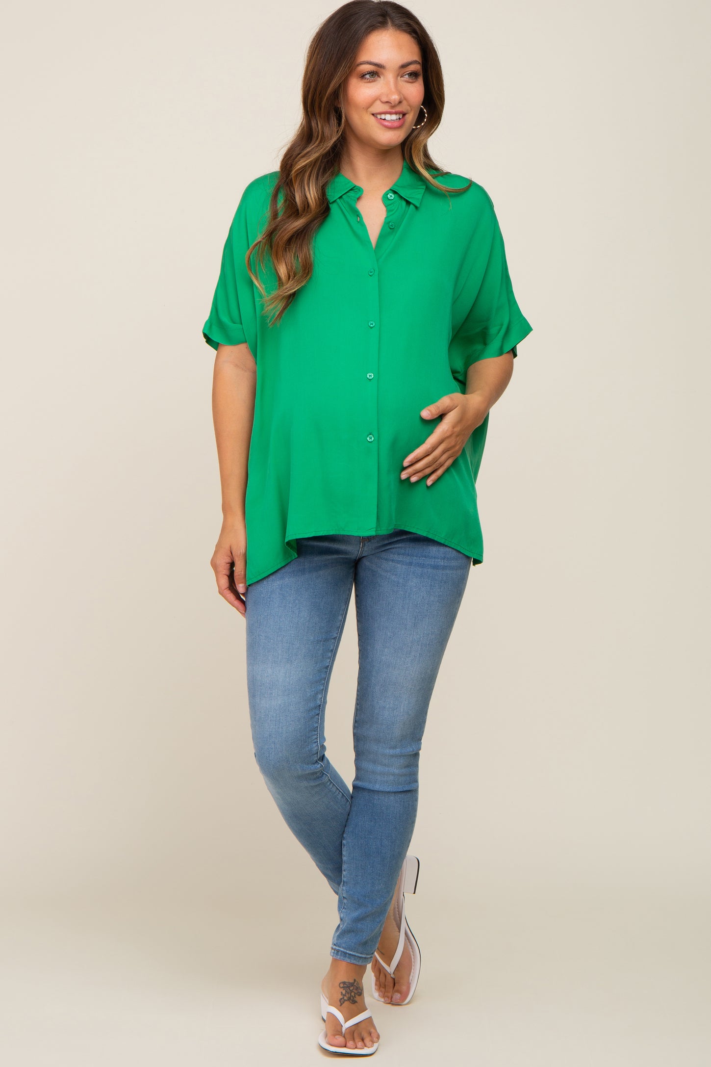 woman wearing a bright green short sleeve maternity blouse and holding her baby bump with blue skinny jeans