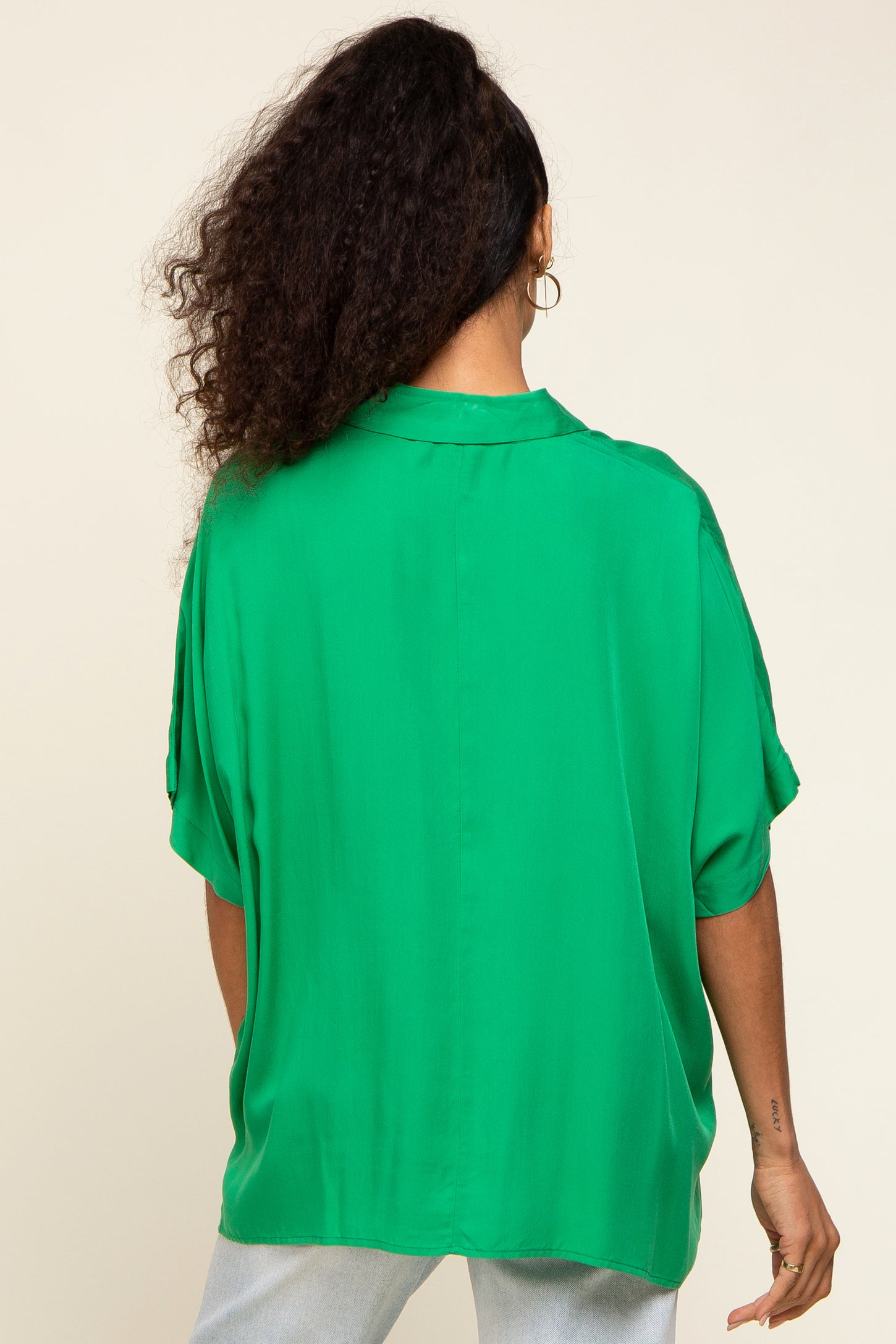 woman wearing a flowy green oversized blouse with short sleeves and a relaxed fit, viewed from the back