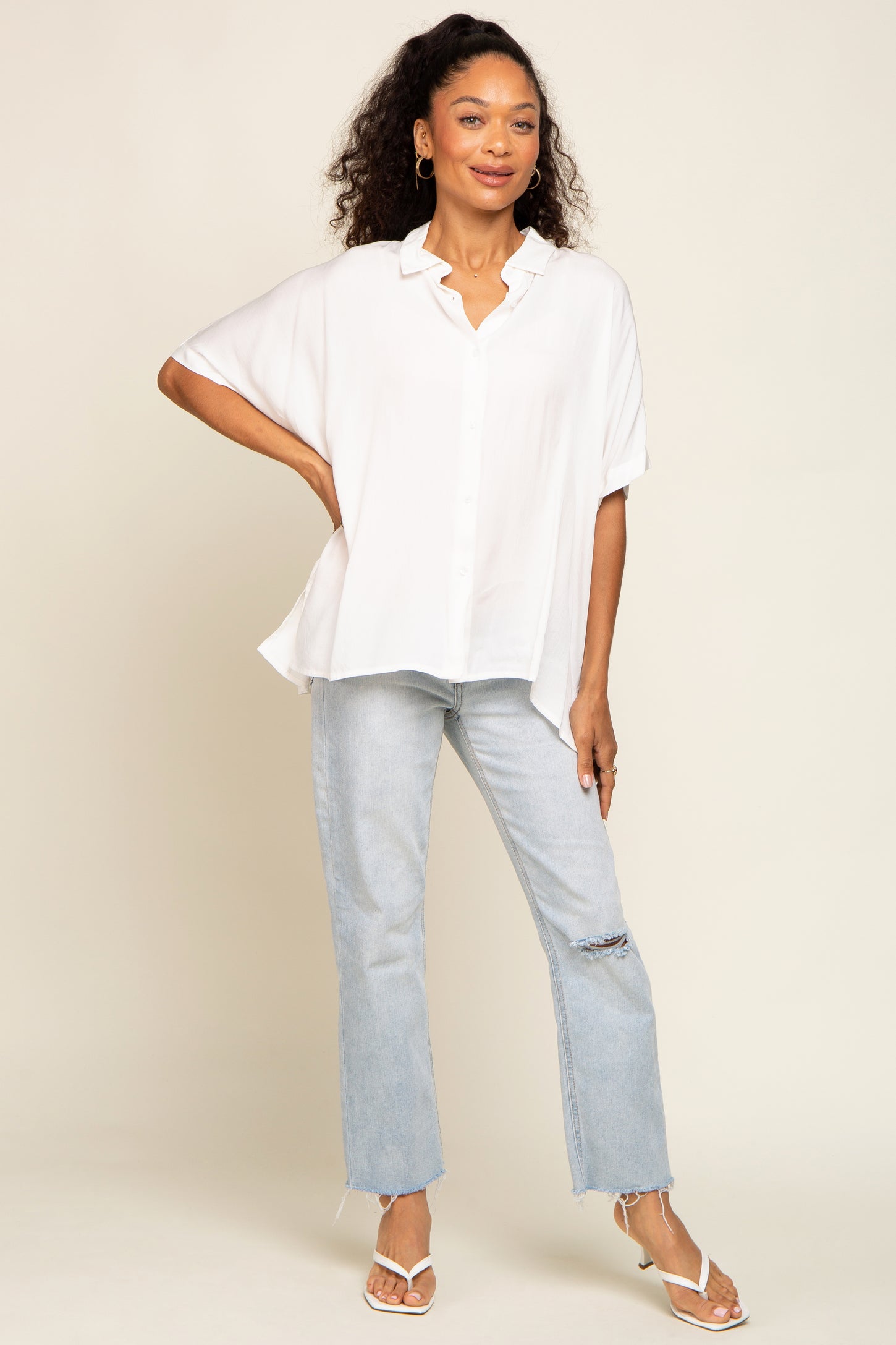 woman wearing a white button-up short sleeve shirt paired with light blue ripped jeans and white sandals
