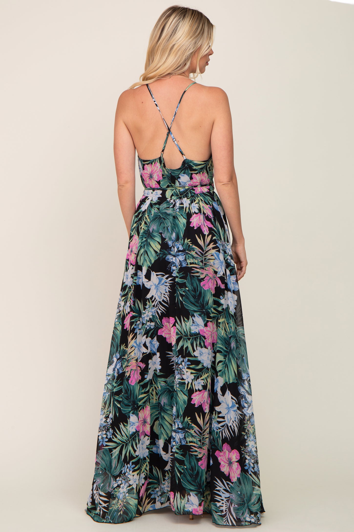 woman wearing a black floral maxi dress with spaghetti straps, showing a vibrant tropical print and a flowy silhouette