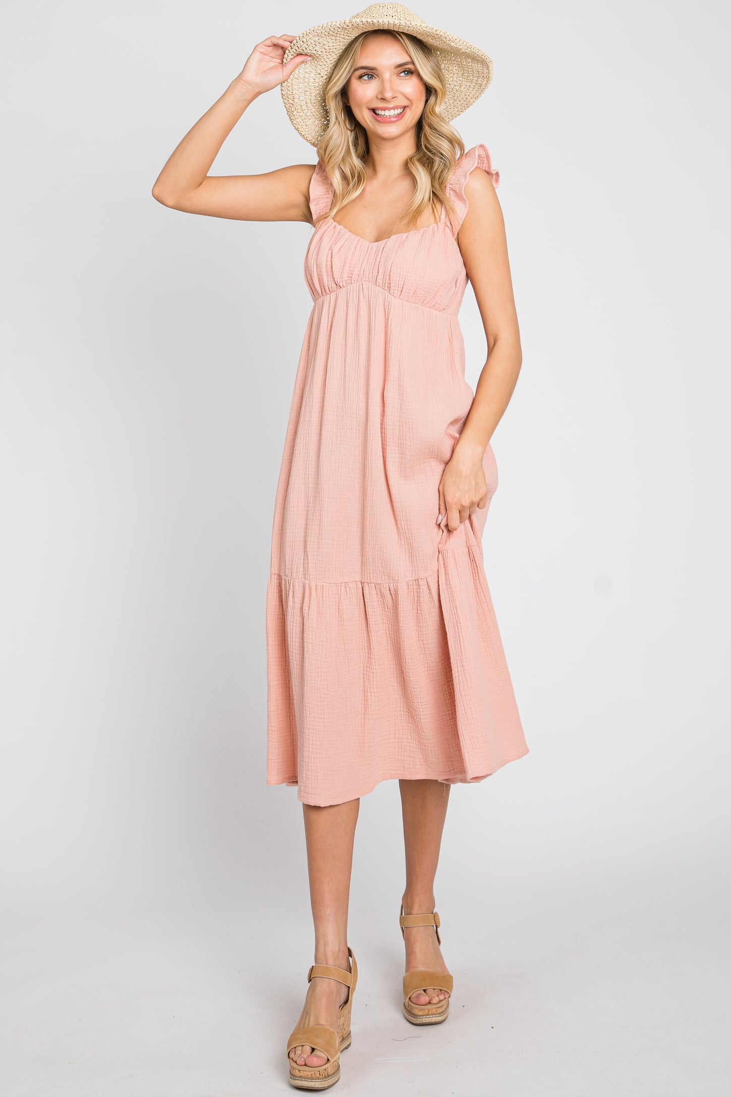 woman wearing a pink ruffled midi dress and straw sun hat with tan wedge sandals