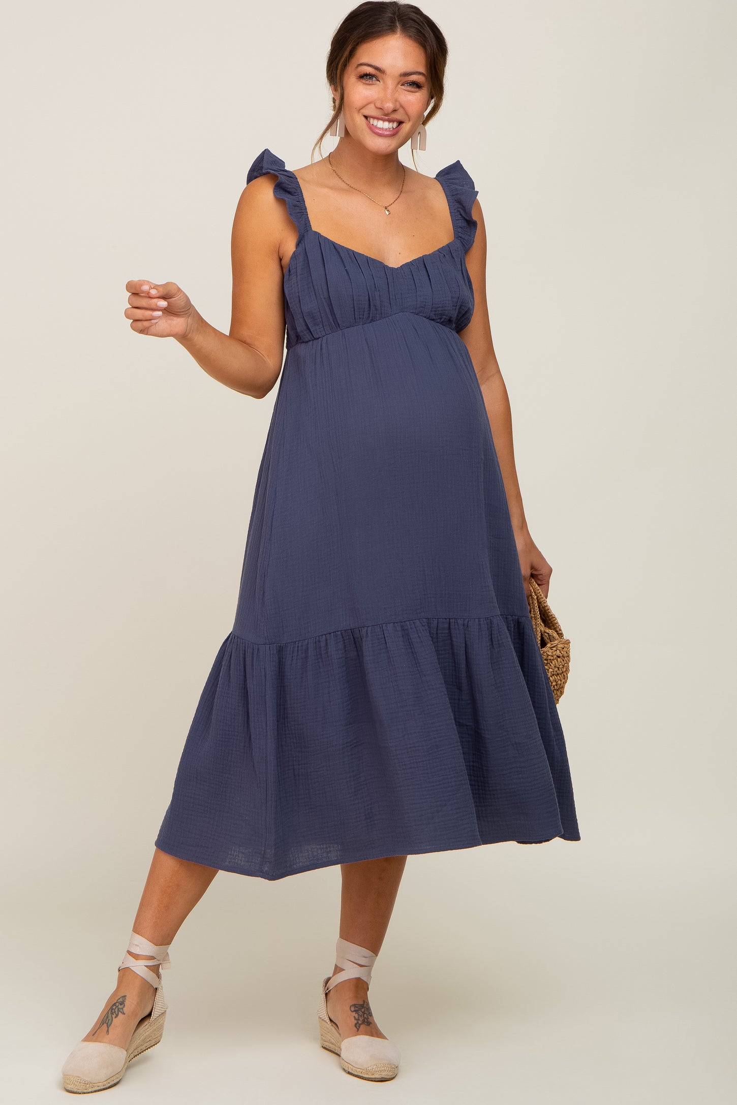 woman wearing a navy blue maternity dress with ruffled straps and a tiered skirt, showcasing her baby bump