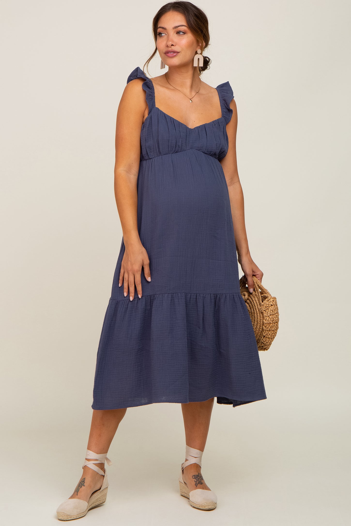 woman wearing a navy blue maternity dress with ruffled straps and a tiered skirt, showcasing her baby bump