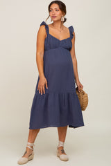 woman wearing a navy blue maternity dress with ruffled straps and a tiered skirt, showcasing her baby bump