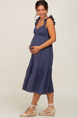 woman wearing a navy blue maternity dress with ruffled straps and a tiered skirt, gently cradling her baby bump