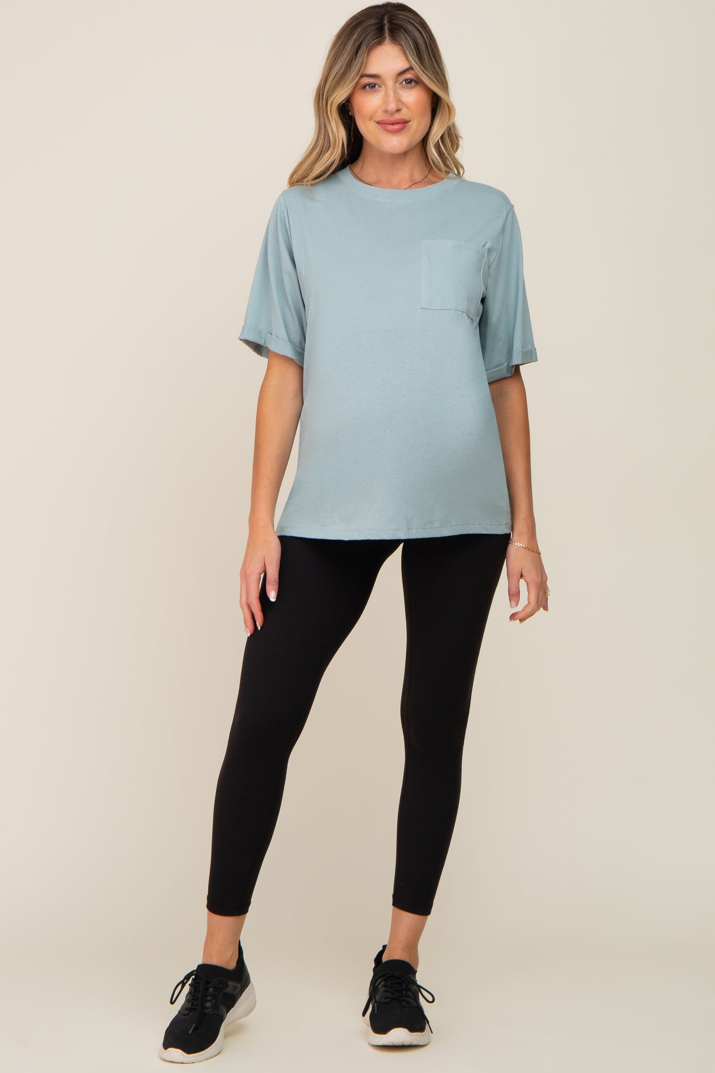 woman wearing a light blue maternity t-shirt with a pocket and black leggings, standing and smiling