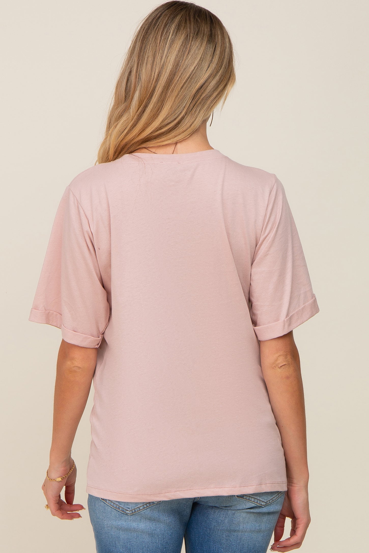 woman wearing a pink short sleeve maternity top, showing the back view, styled with rolled sleeves