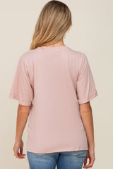 woman wearing a pink short sleeve maternity top, showing the back view, styled with rolled sleeves