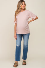 woman wearing a light pink maternity top with a pocket and distressed blue jeans, showcasing her baby bump