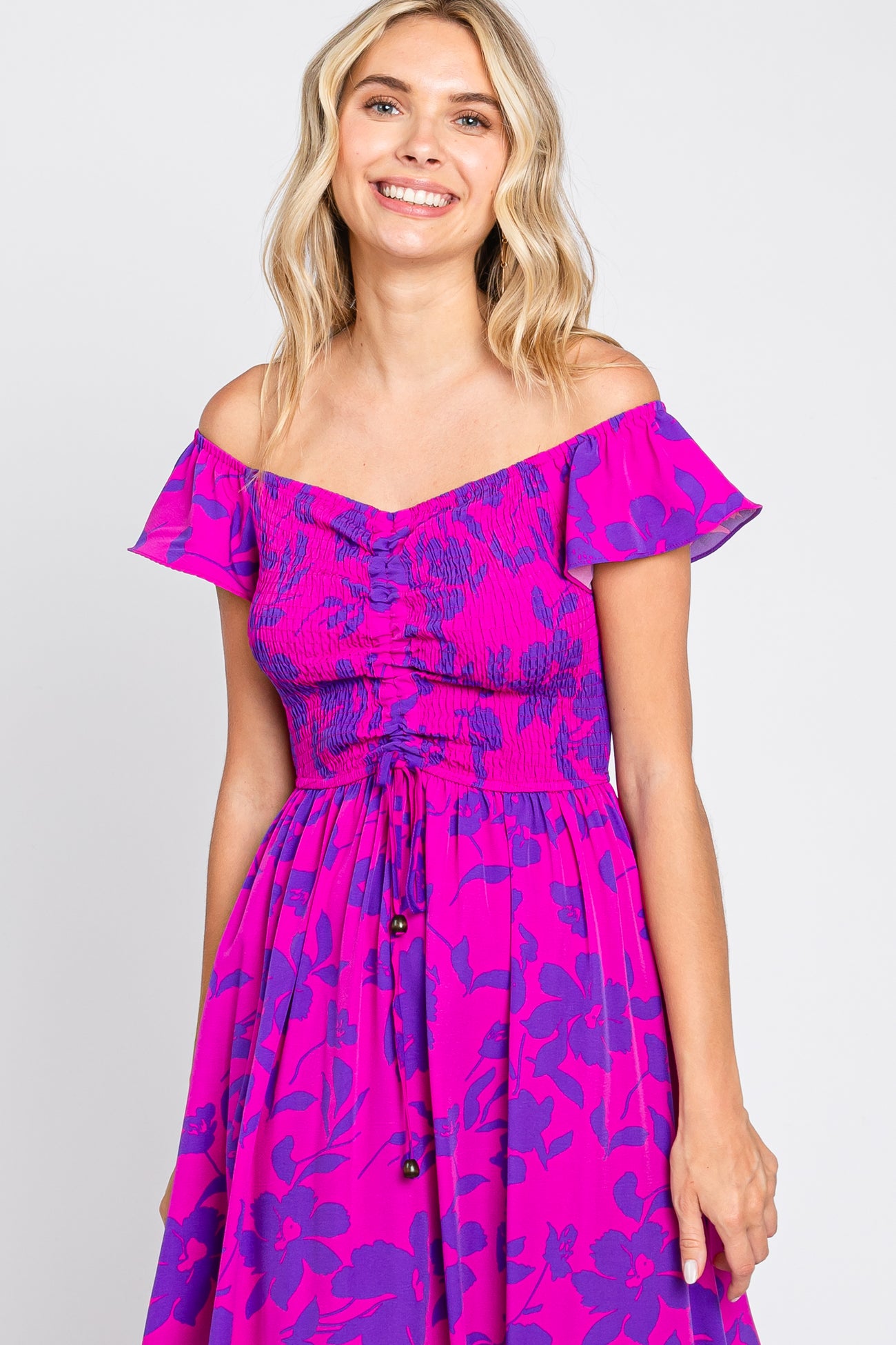 woman wearing a pink off-the-shoulder floral dress with a smocked bodice and button details