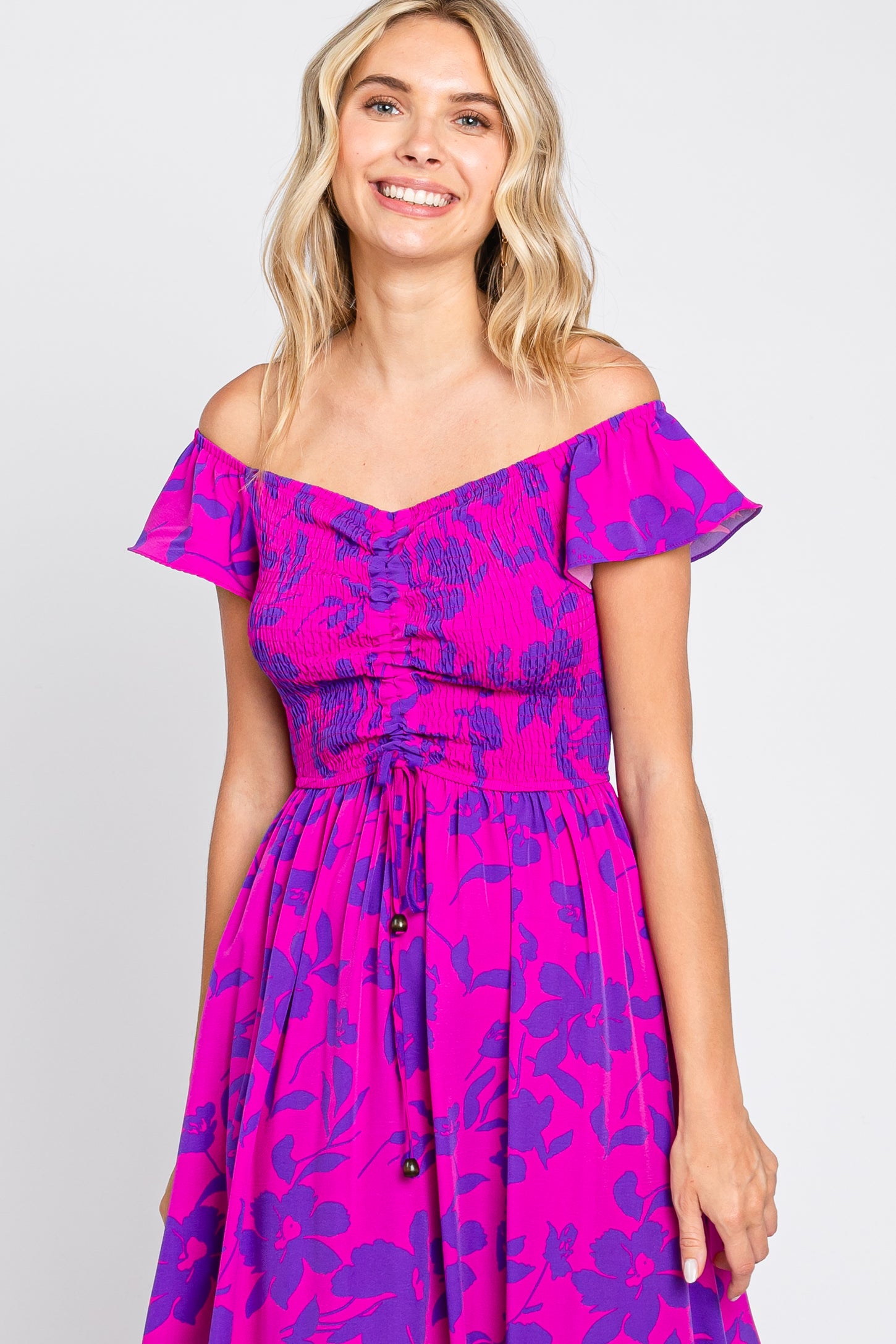 woman wearing a pink off-the-shoulder floral dress with a smocked bodice and button details