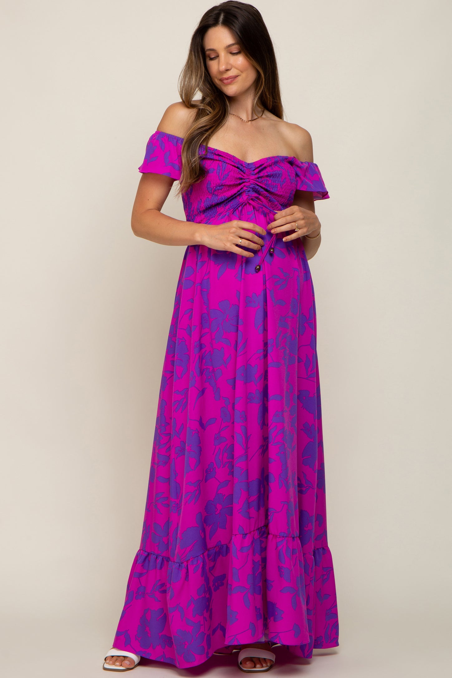 woman wearing a purple off-shoulder maternity maxi dress with gathered detailing and a flowy skirt, holding her baby bump