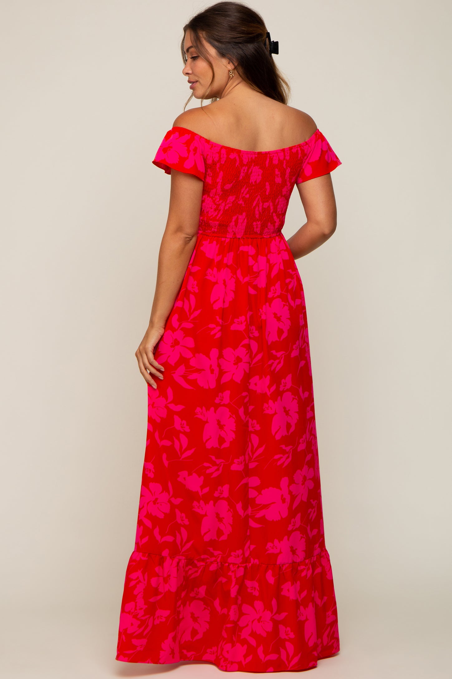 woman wearing a floral off-shoulder maternity maxi dress in bright pink and red, showing a fitted bodice and flared skirt