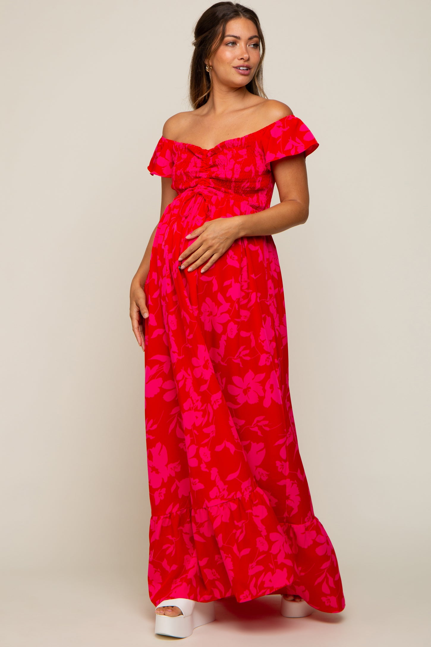woman wearing a red floral off-the-shoulder maternity maxi dress and holding her baby bump