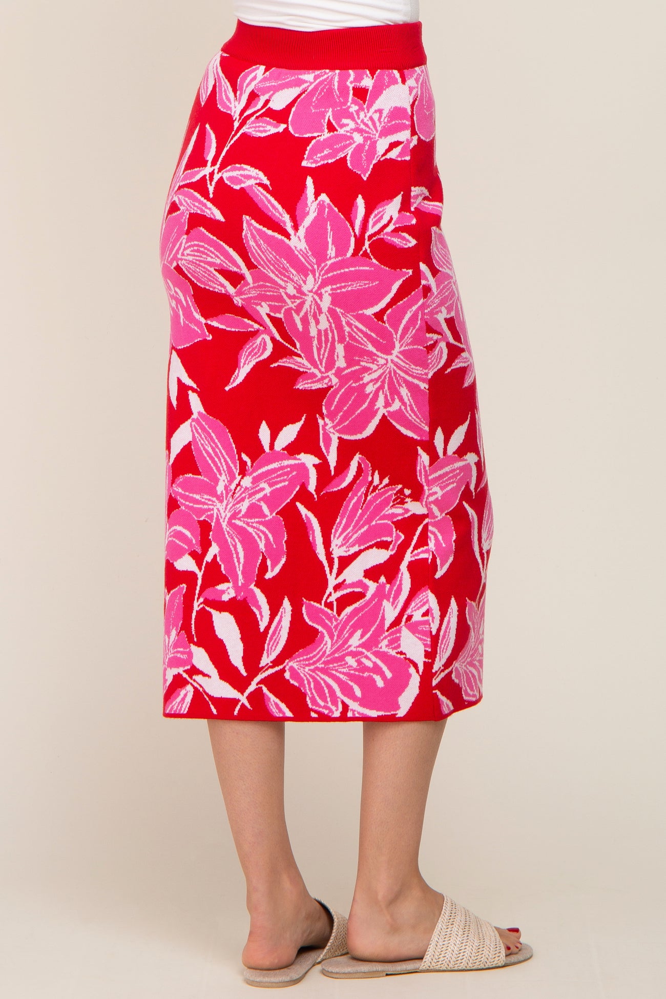 woman wearing a red floral midi skirt with pink and white leaf patterns, styled with beige slip-on sandals
