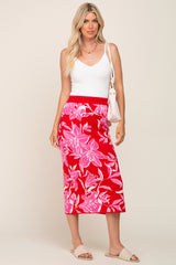 woman wearing a white v-neck tank top and a red floral midi skirt, holding a white handbag, standing on a beige background