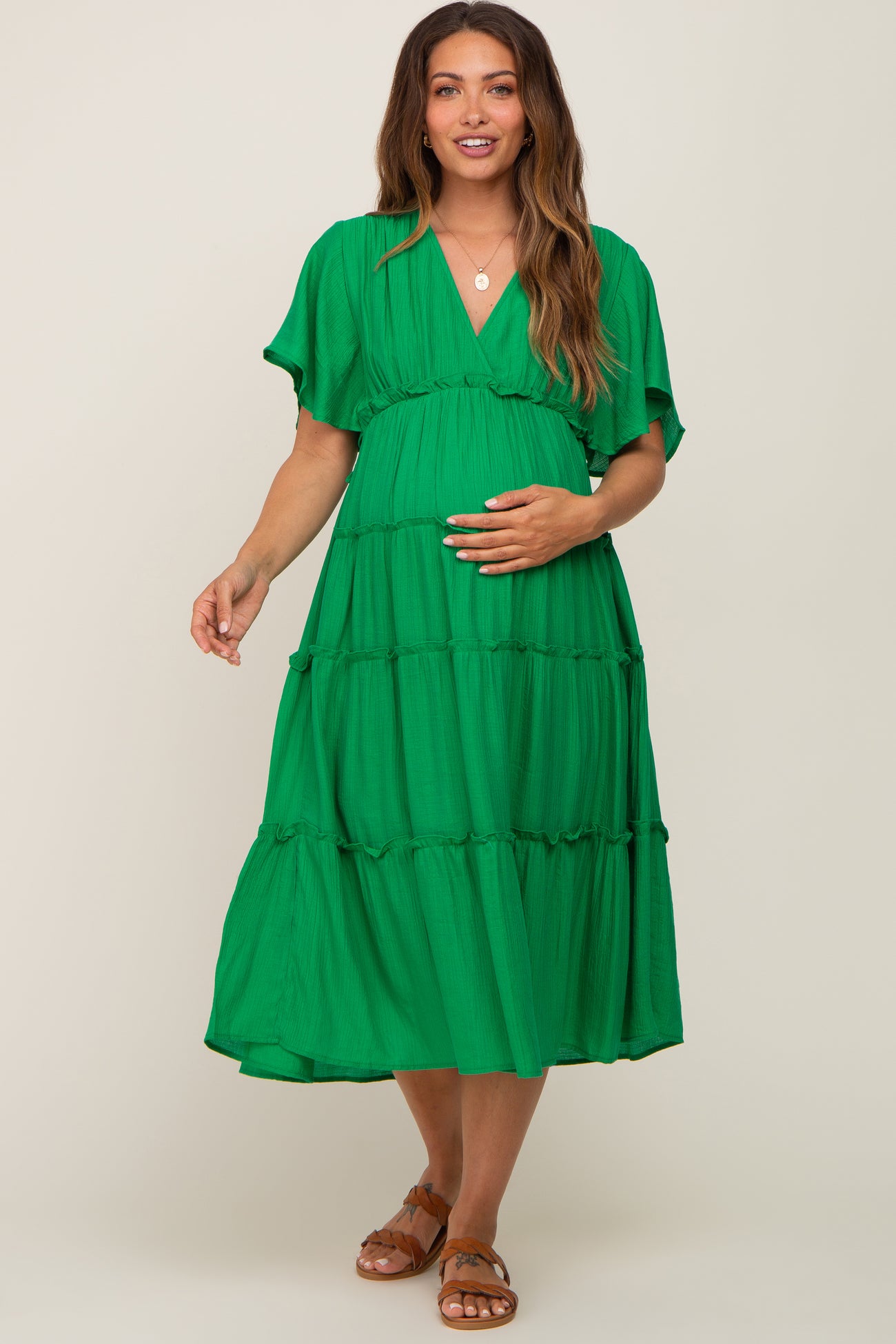 pregnant woman wearing a green tiered maternity midi dress with short flutter sleeves and brown sandals