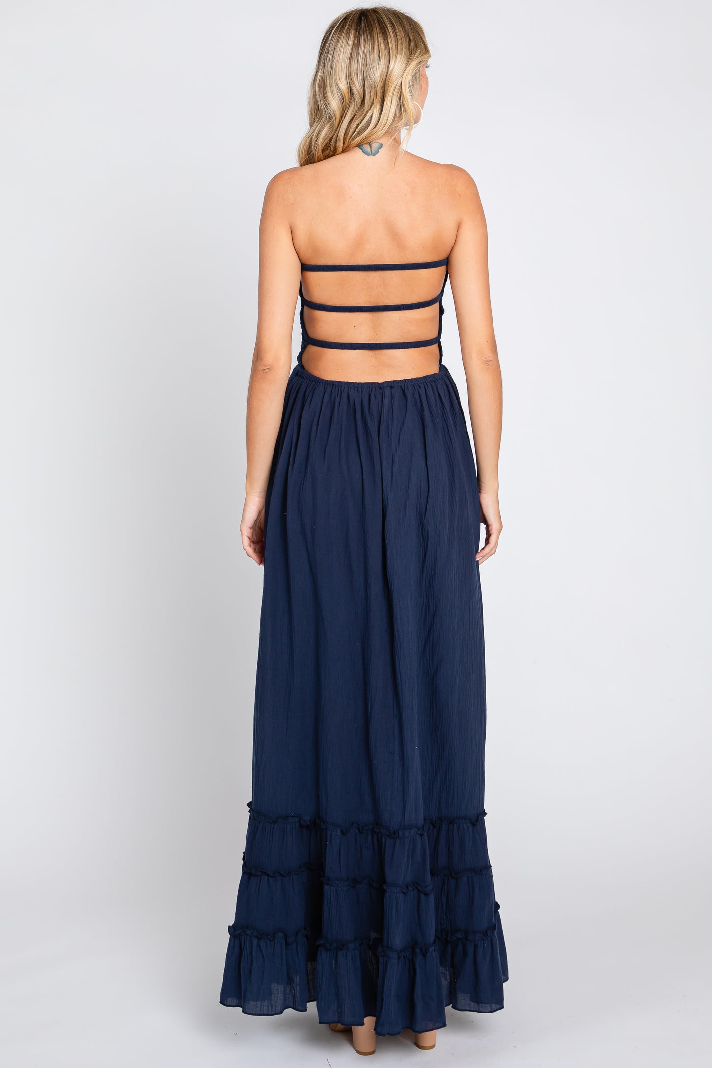 back view of woman wearing navy blue strapless maxi dress with tiered ruffle hem and open strappy back