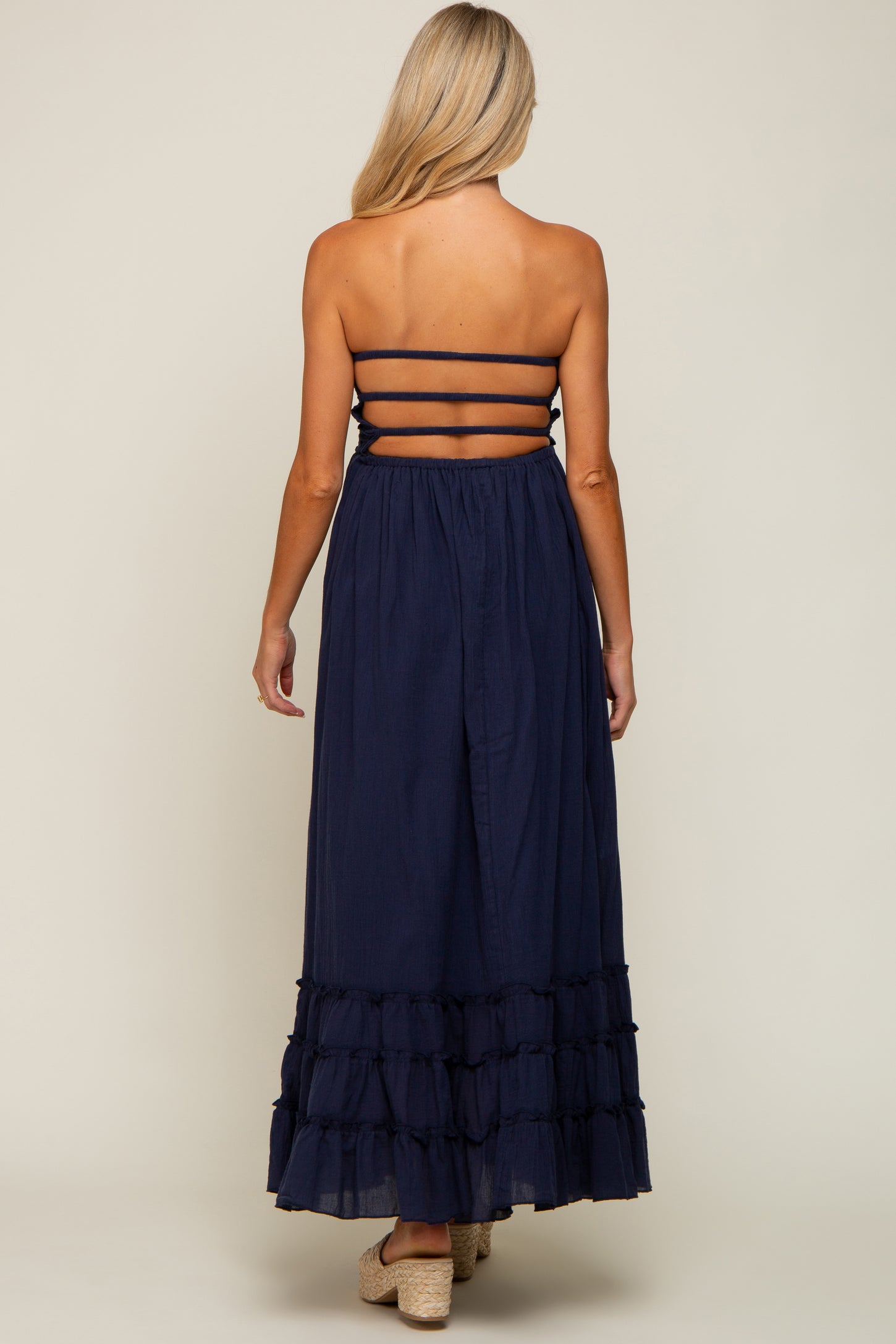 Back view of a woman wearing a navy blue strapless maxi dress with a tiered ruffle hem and horizontal back straps
