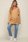 Pregnant woman wearing a tan waffle knit maternity sweater and blue jeans with white sneakers