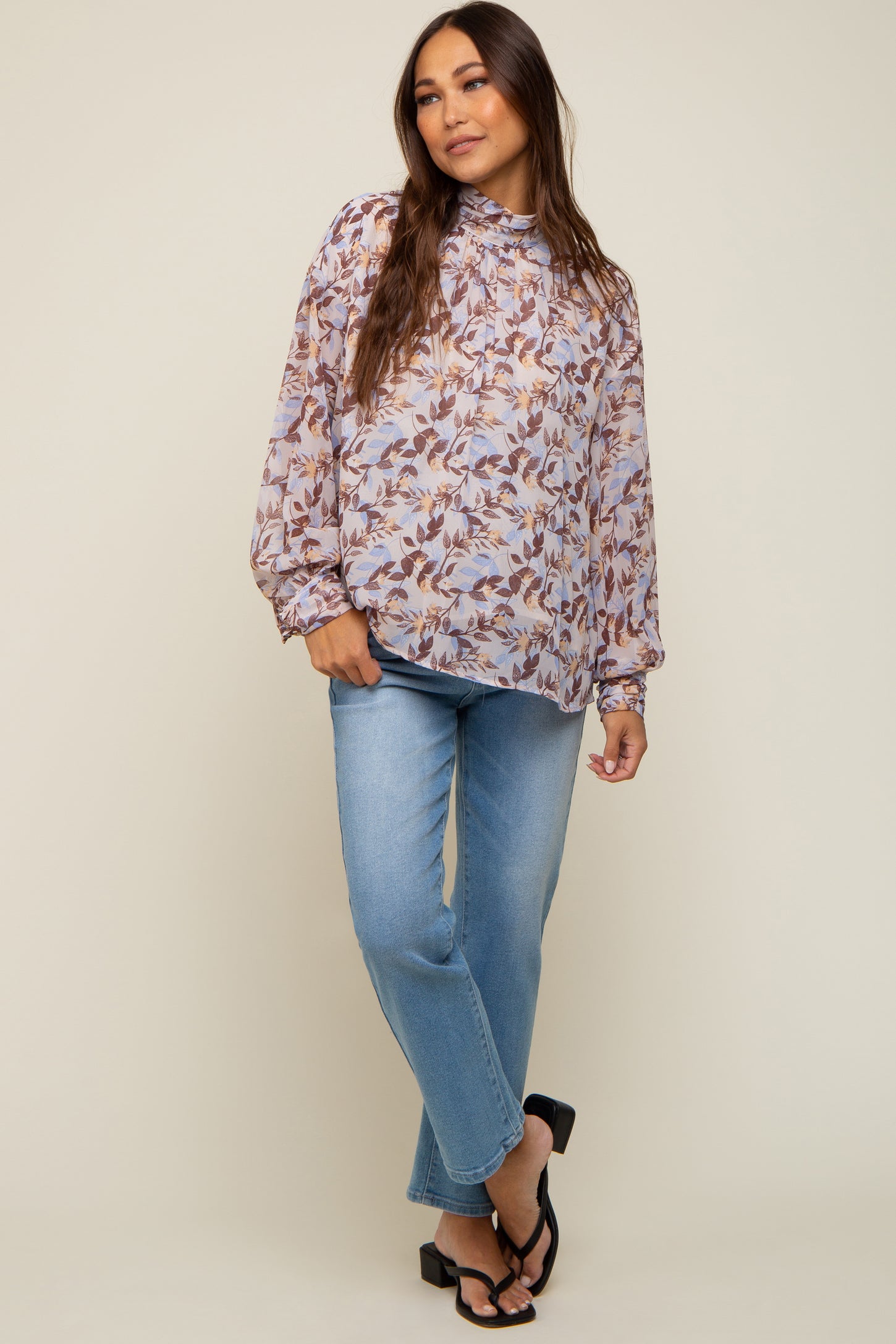 Woman wearing a floral high-neck long sleeve blouse and light wash straight leg jeans with black sandals