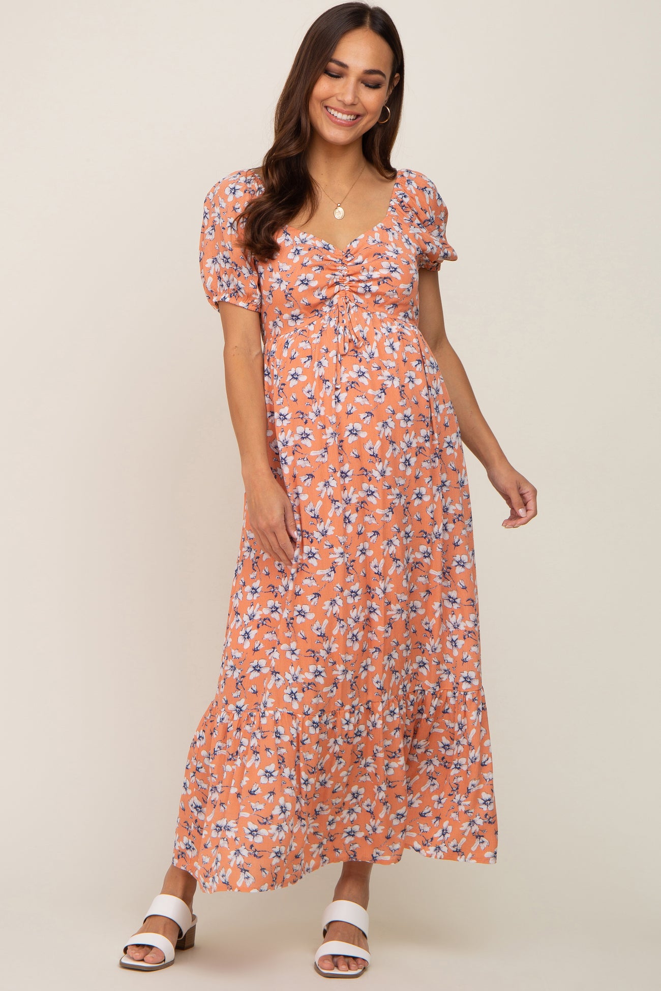 woman wearing an orange floral maternity maxi dress with puff sleeves and a gathered front, showcasing a baby bump