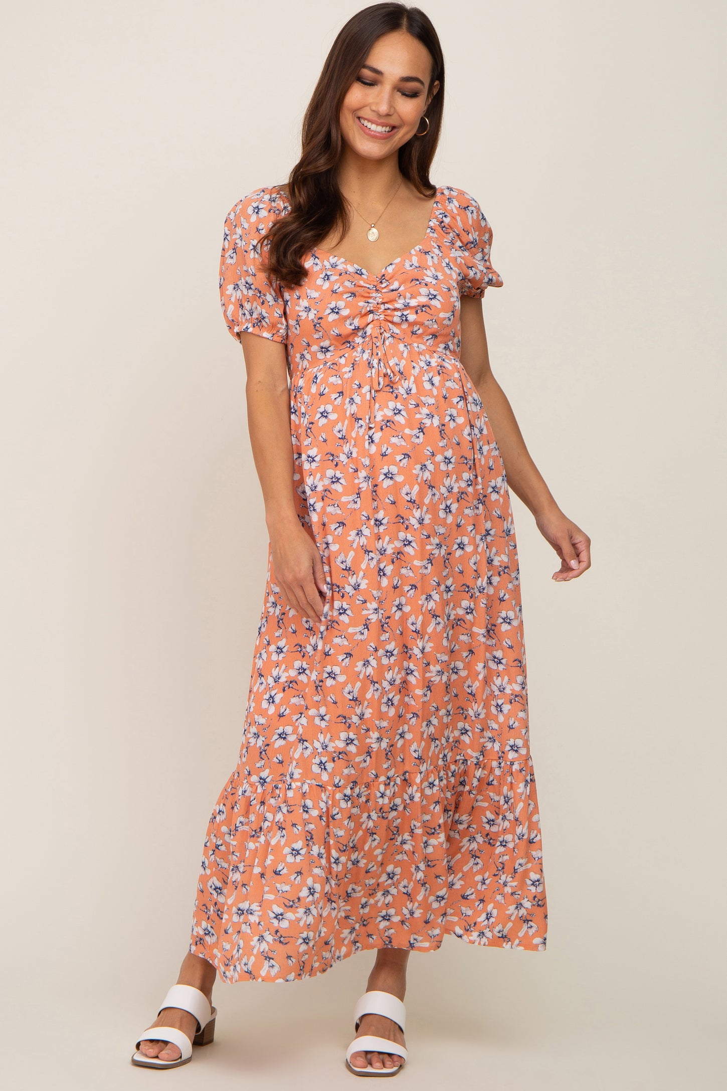 woman wearing an orange floral maternity maxi dress with puff sleeves and a gathered front, showcasing a baby bump