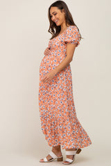 woman wearing an orange floral maternity maxi dress and holding her baby bump