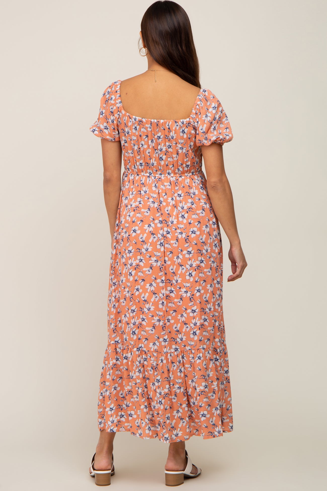 woman wearing a floral orange maternity maxi dress with puff sleeves and a tiered hem, showing a baby bump