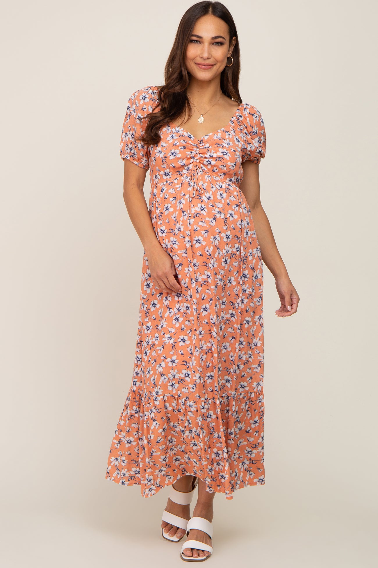 woman wearing a coral floral maternity maxi dress with puff sleeves and a cinched bodice, showing her baby bump