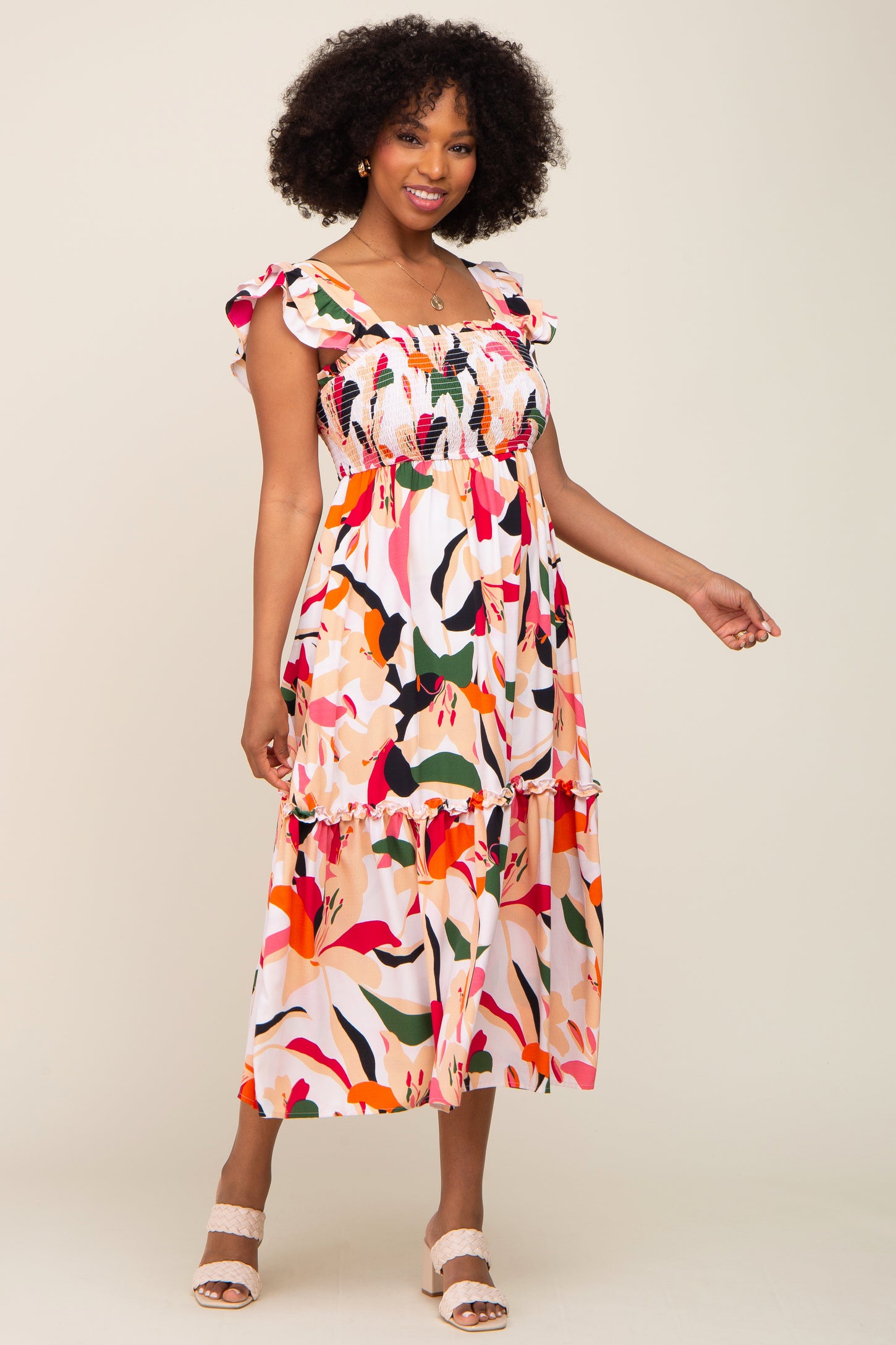 Woman wearing a colorful floral smocked midi dress with ruffle sleeves and cream block heel sandals