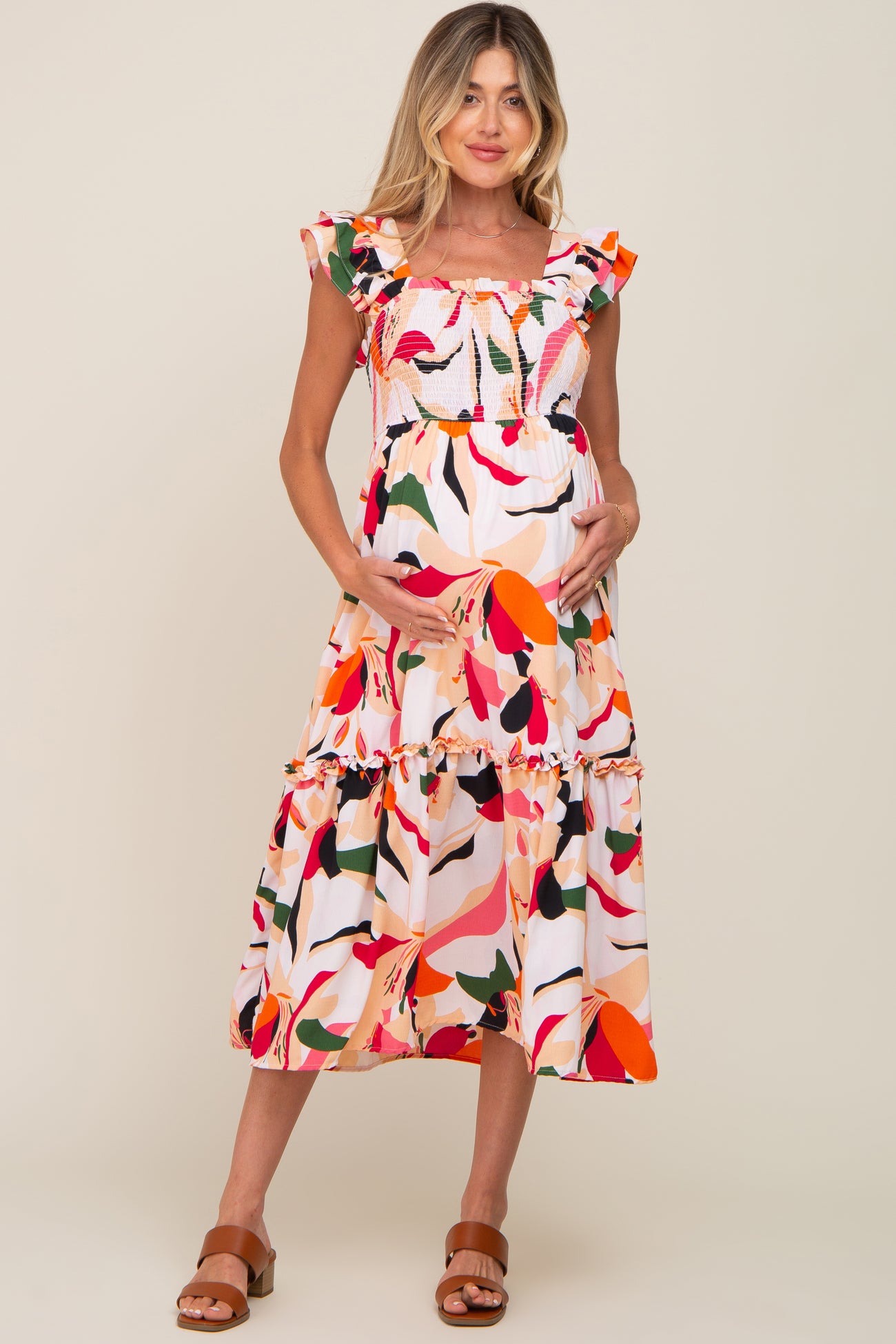 pregnant woman in a colorful floral smocked maternity midi dress with ruffle sleeves and brown sandals