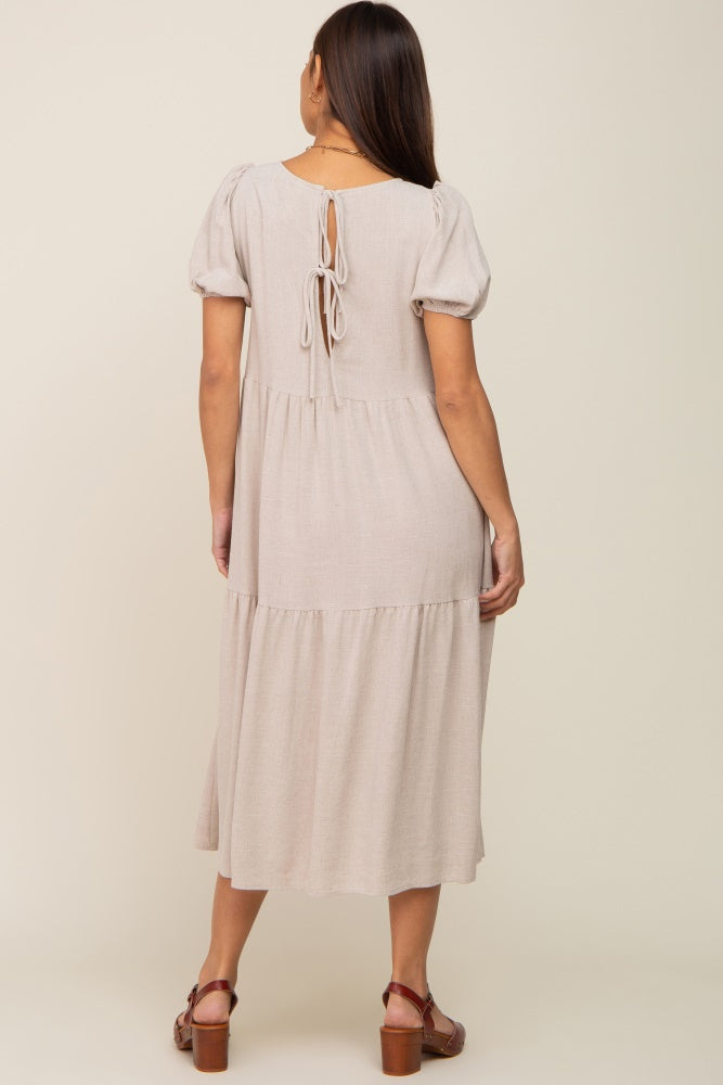 Back view of a woman wearing a beige tiered midi dress with puff sleeves and a tie-back detail.