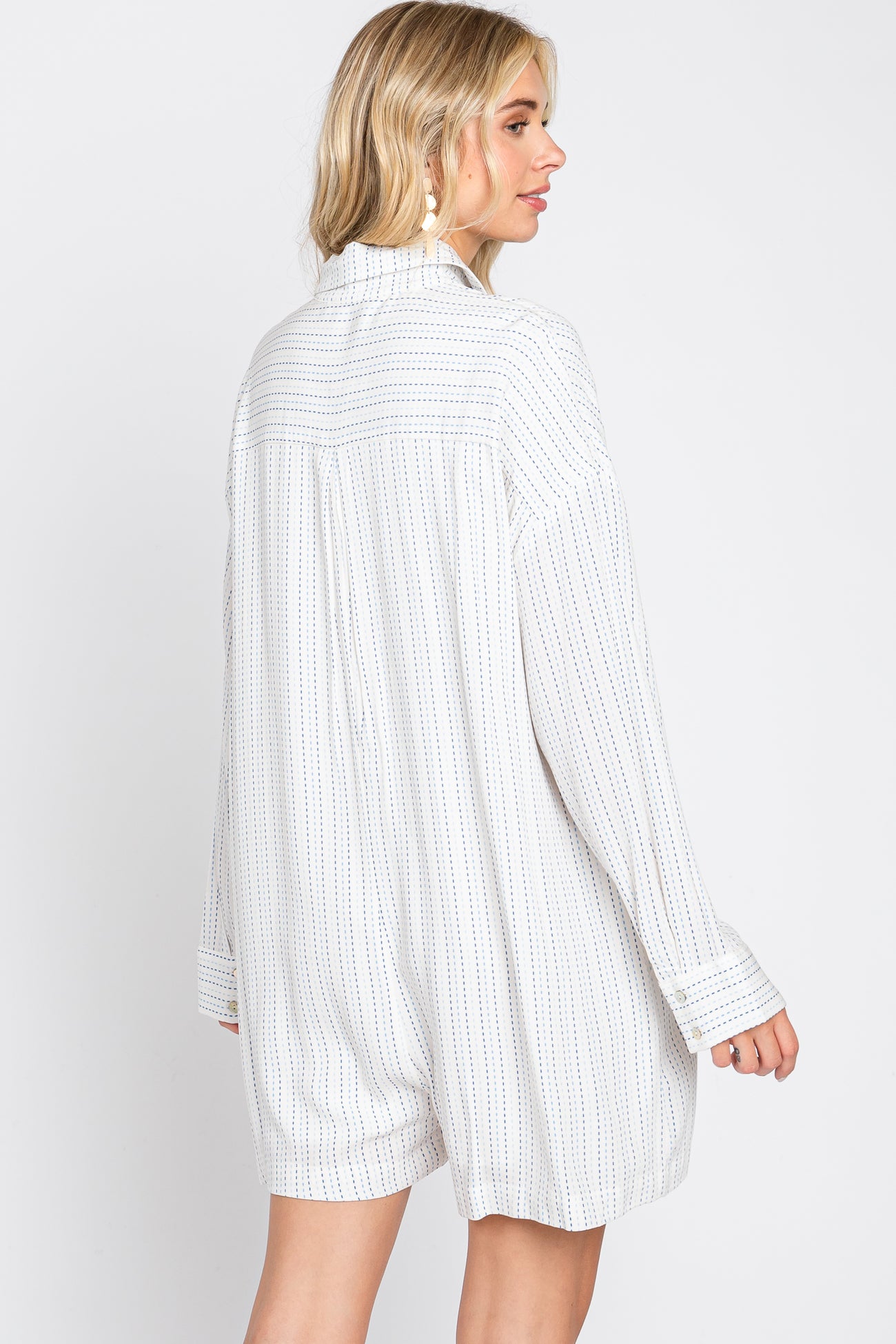 Woman wearing a white oversized button-down shirt with blue vertical pinstripes and matching shorts