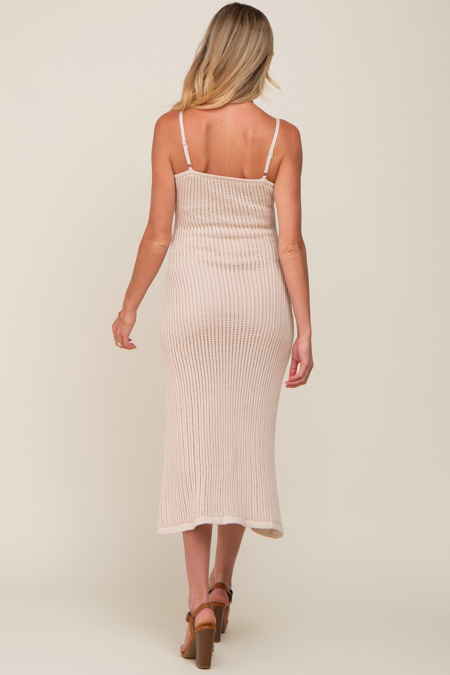 back view of woman wearing beige ribbed knit midi dress with spaghetti straps and brown heels