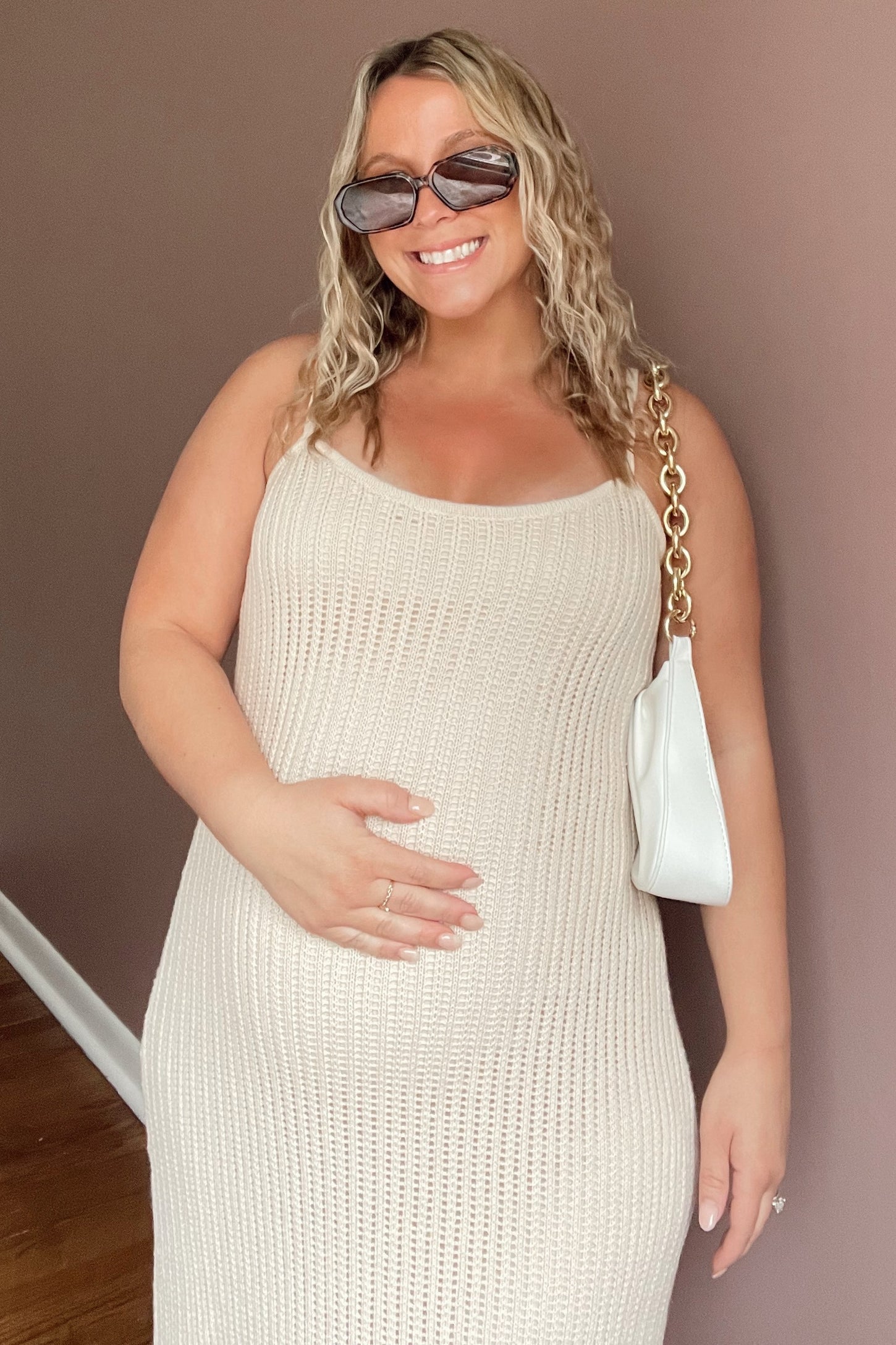smiling pregnant woman in cream crochet maternity dress with white gold chain shoulder bag