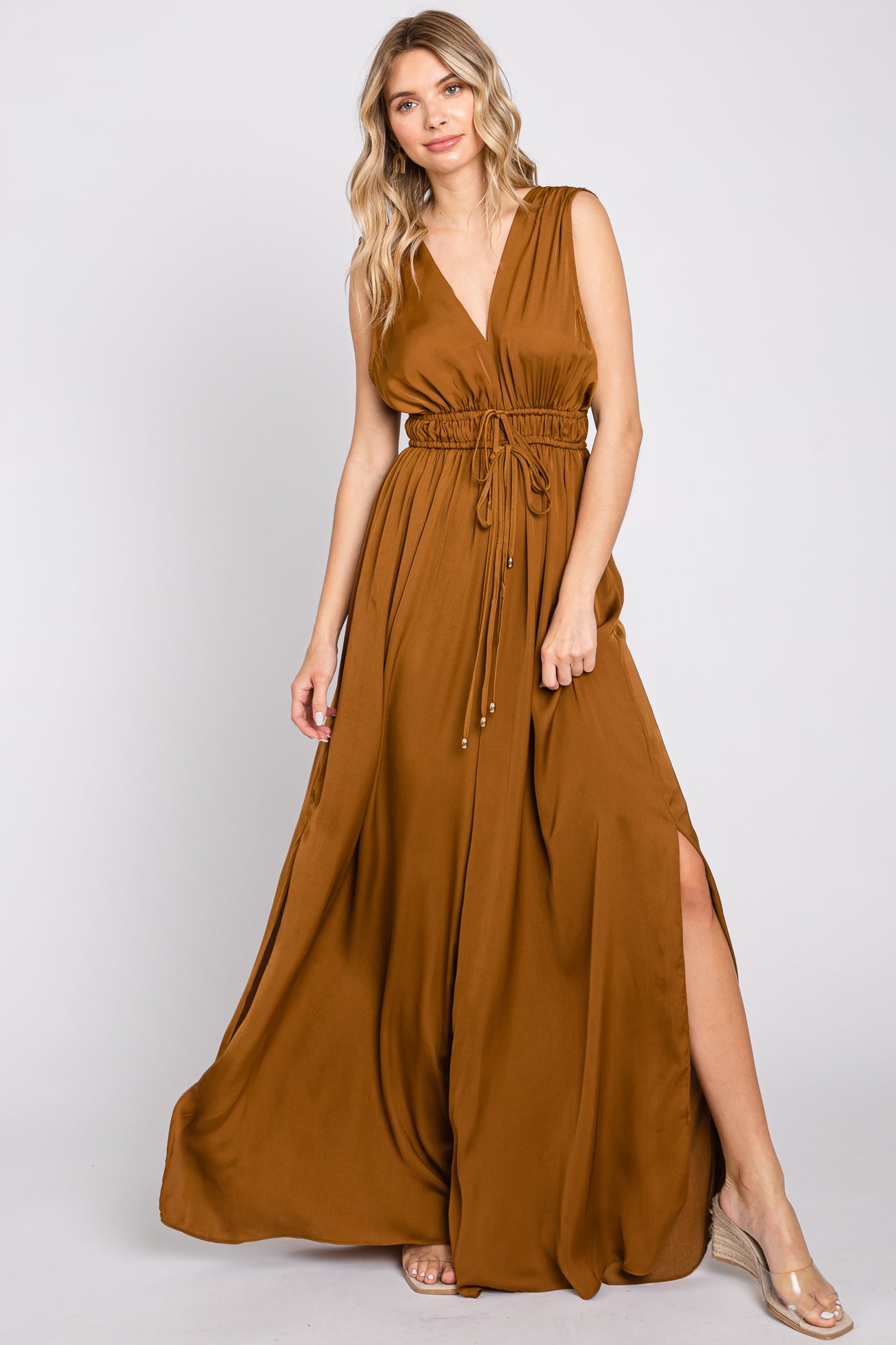 Woman wearing a sleeveless bronze satin maxi dress with a drawstring waist and side slit