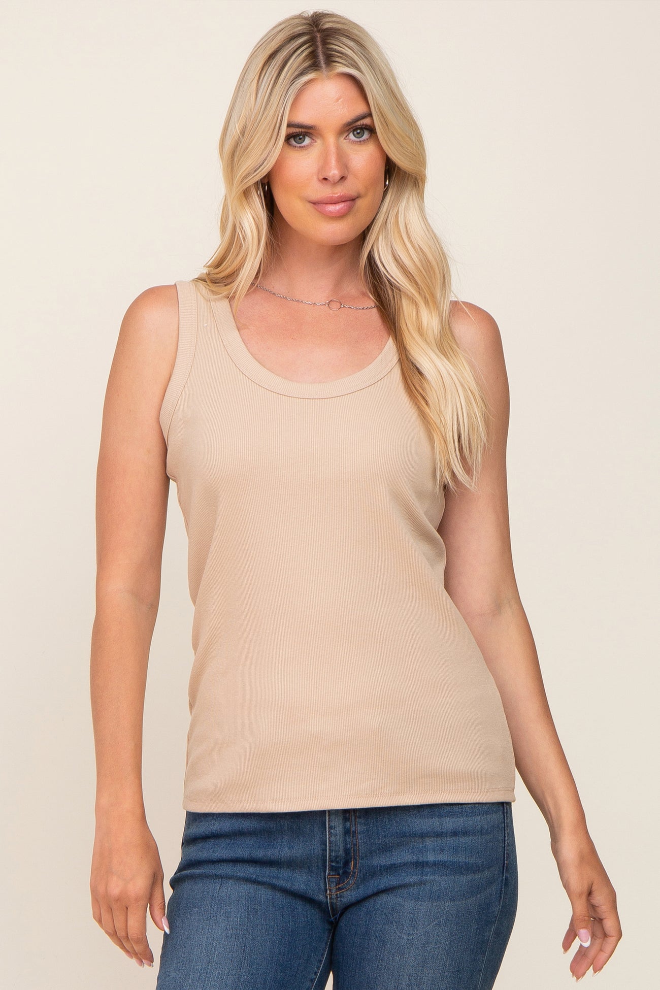 woman wearing a light beige ribbed sleeveless top with a scoop neckline, paired with blue jeans