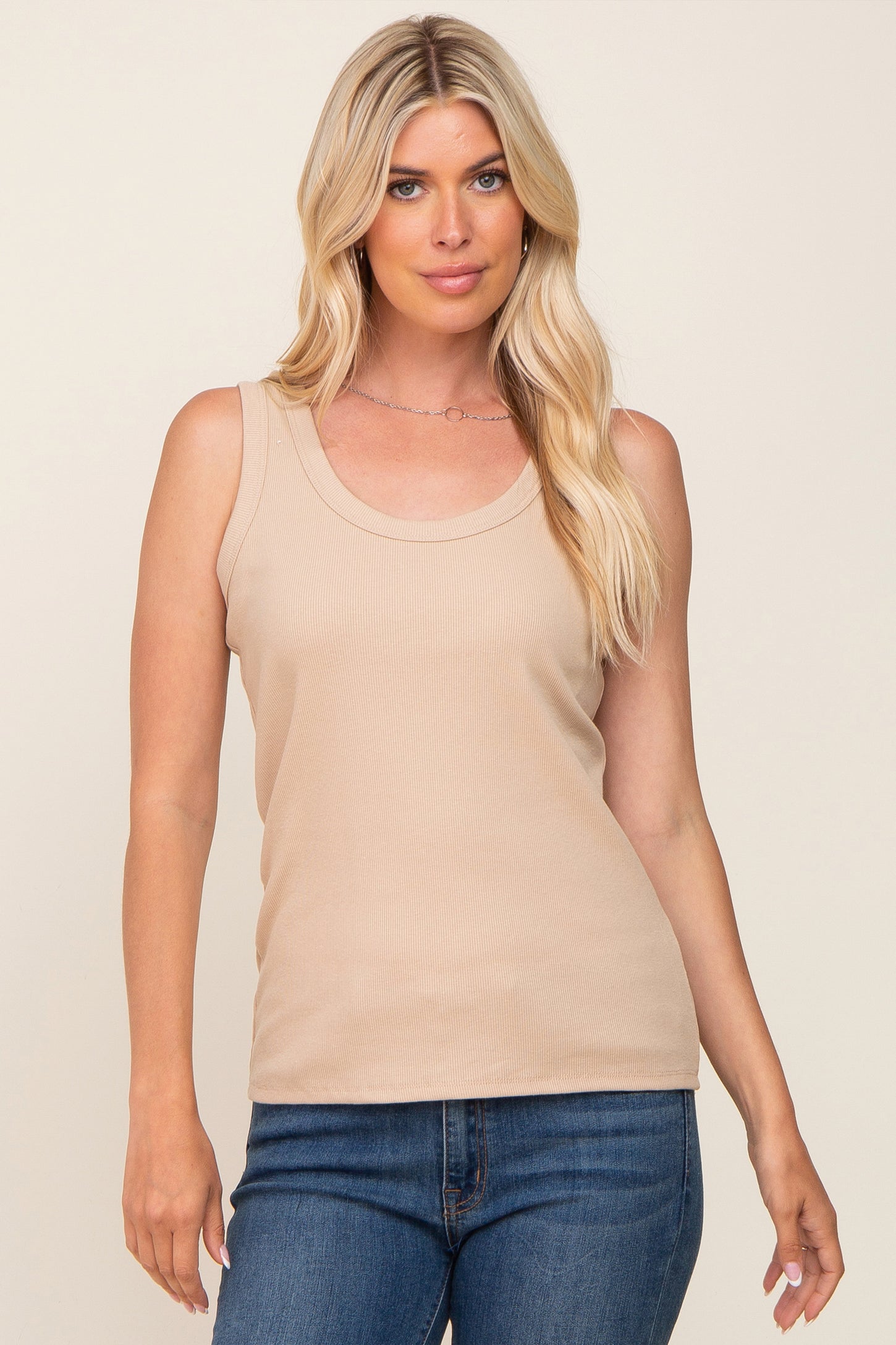 woman wearing a light beige ribbed sleeveless top with a scoop neckline, paired with blue jeans