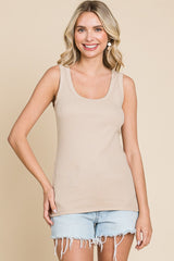 woman wearing a beige ribbed tank top and light blue denim shorts, smiling against a neutral background