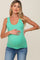 woman wearing a teal maternity tank top and holding her baby bump while posing in a relaxed manner