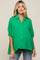 Woman wearing a green oversized button-down gauze shirt and blue jeans against a neutral background