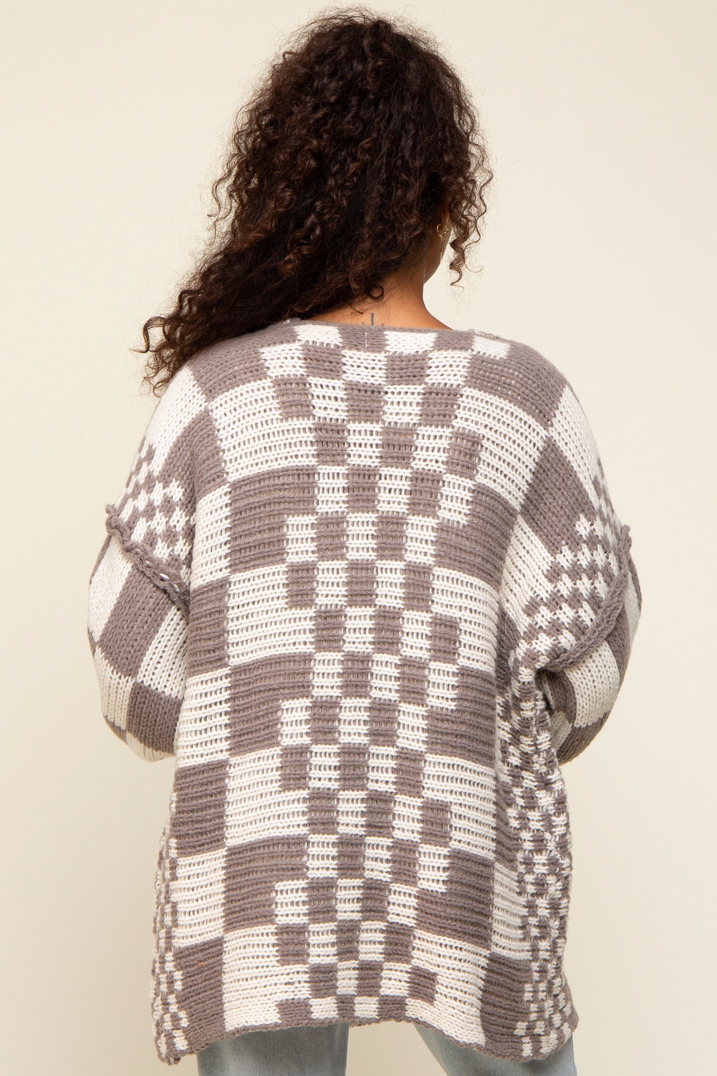 Back view of a person with curly hair wearing a brown and white checkered oversized knit cardigan