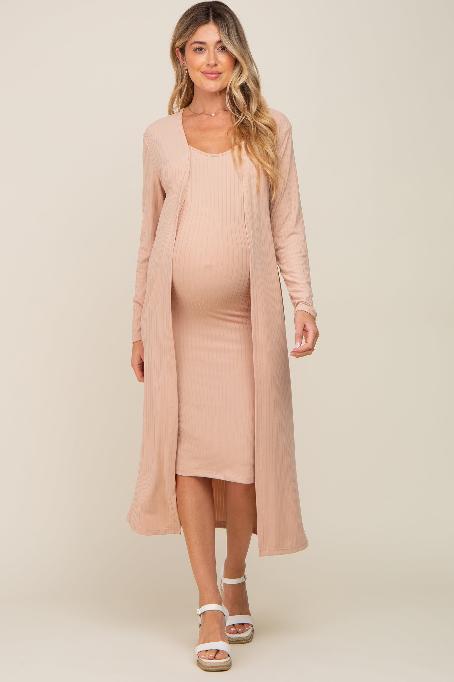 woman wearing a light peach maternity dress with a matching open-front cardigan and showing her baby bump