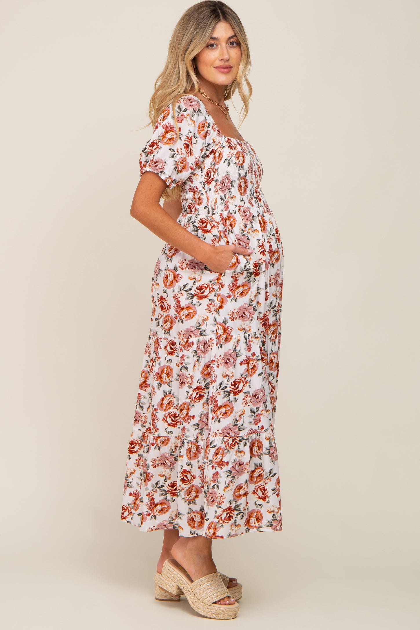woman wearing a white floral maternity dress with short sleeves and pockets, showing her baby bump