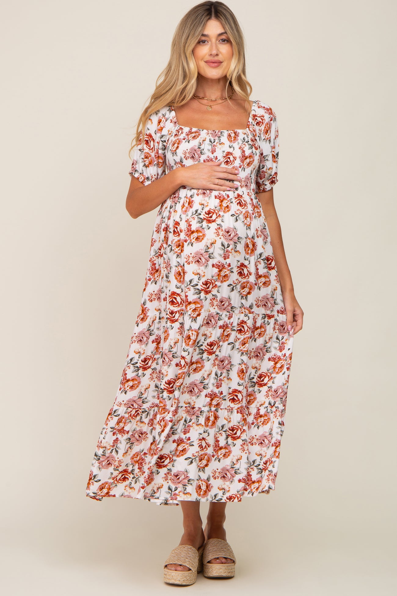 woman wearing a white floral maternity maxi dress with square neckline and puff sleeves, holding her baby bump