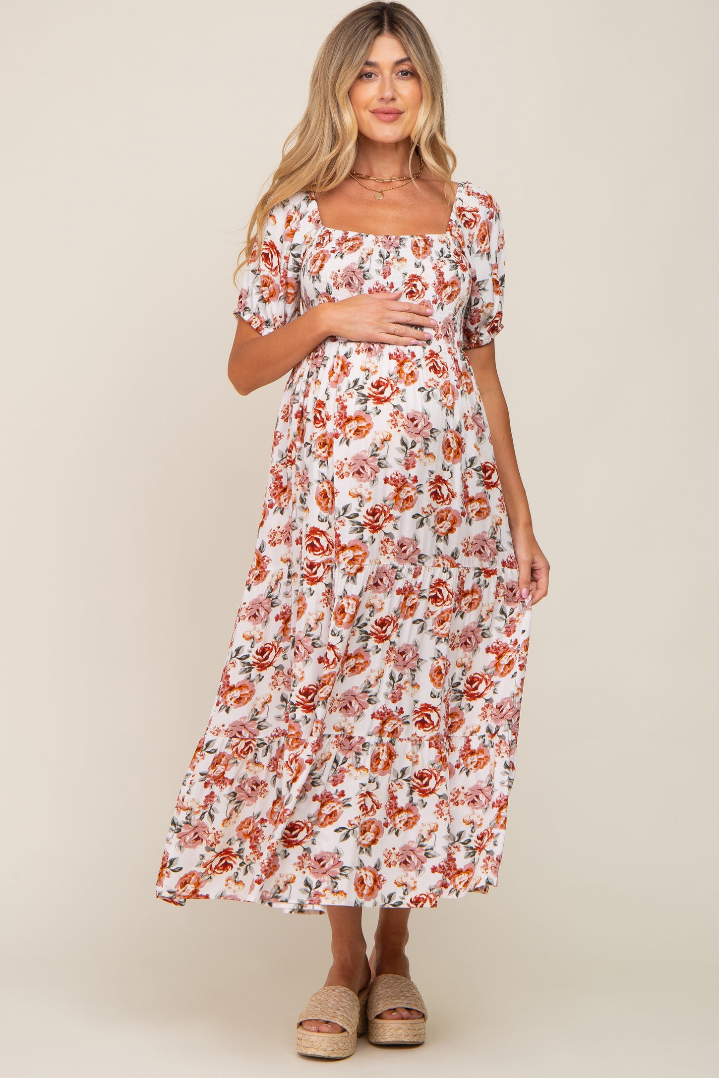 woman wearing a white floral maternity maxi dress with square neckline and puff sleeves, holding her baby bump