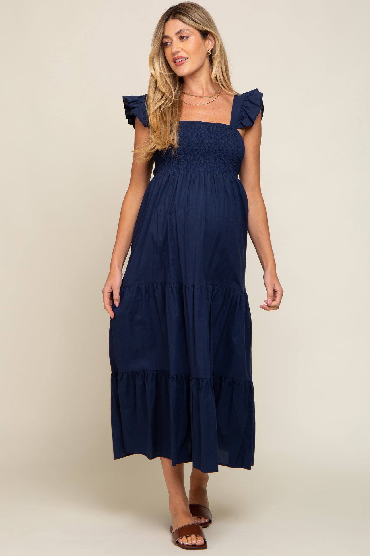 woman wearing a navy blue maternity dress with ruffled sleeves and a tiered skirt, showcasing her baby bump